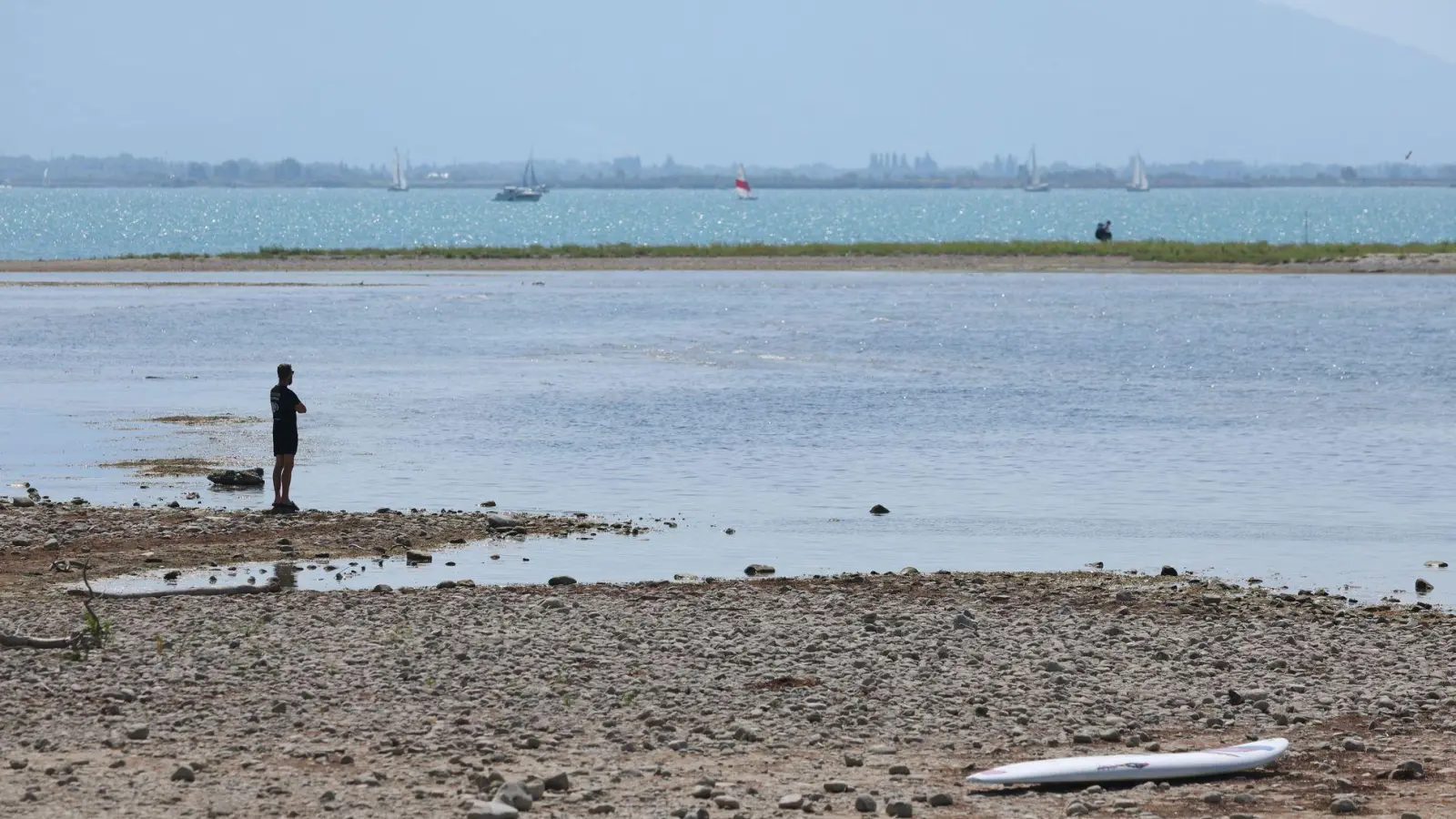 Es bleibt heiß in Bayern: Ein Mann steht am trockenen Ufer des Bodensees neben einem Surfboard. (Archivbild) (Foto: Karl-Josef Hildenbrand/dpa)