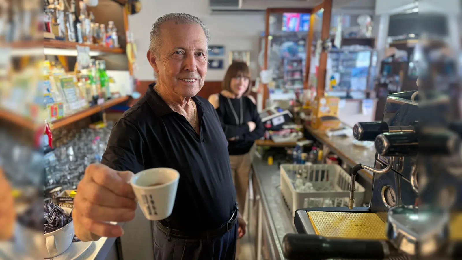 Orlando Paldino zeigt stolz eine Tasse Espresso für 70 Cent. Im Hintergrund steht seine Frau Rosina Furiati. (Foto: Christoph Sator/dpa)