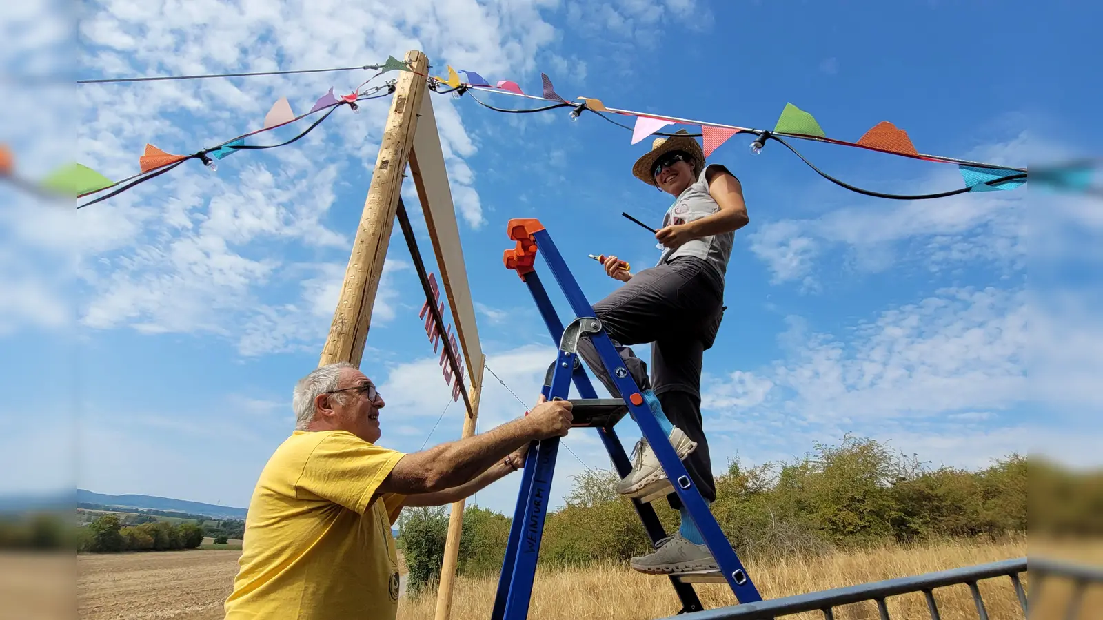 Eleni Martin aus dem P-Seminar ist zugleich Helferin auf dem Festival, genauso wie ihr Vater Uwe Martin. Gemeinsam haben sie die bunten Wimpel und die Lichterkette an den Seiten-Seilen des Torbogens montiert. (Foto: Nina Daebel)