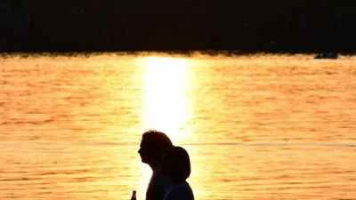 Menschen gehen bei Sonnenuntergang am Ufer des Tegeler Sees in Berlin. (Foto: Sebastian Gollnow/dpa)