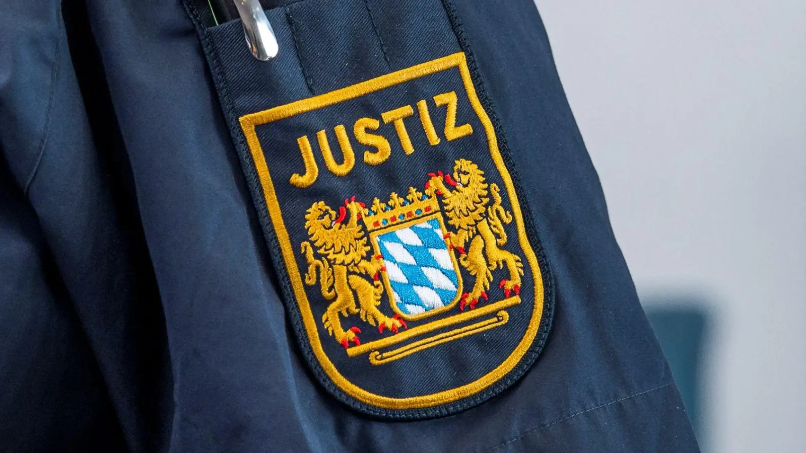 Auf der Uniform eines Justizbeamten ist das Bayerische Wappen und die Aufschrift „Justiz“ zu sehen. Betrüger geben sich immer wieder als falsche Justiz-Mitarbeiter aus. (Symbolbild) (Foto: Daniel Vogl/dpa)