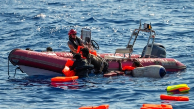 Ein Mitglied der spanischen Nichtregierungsorganisation Open Arms hilft Migranten, an Bord zu kommen. Viele Minderjährige sterben während der Flucht. (Foto: Francisco Seco/AP/dpa)