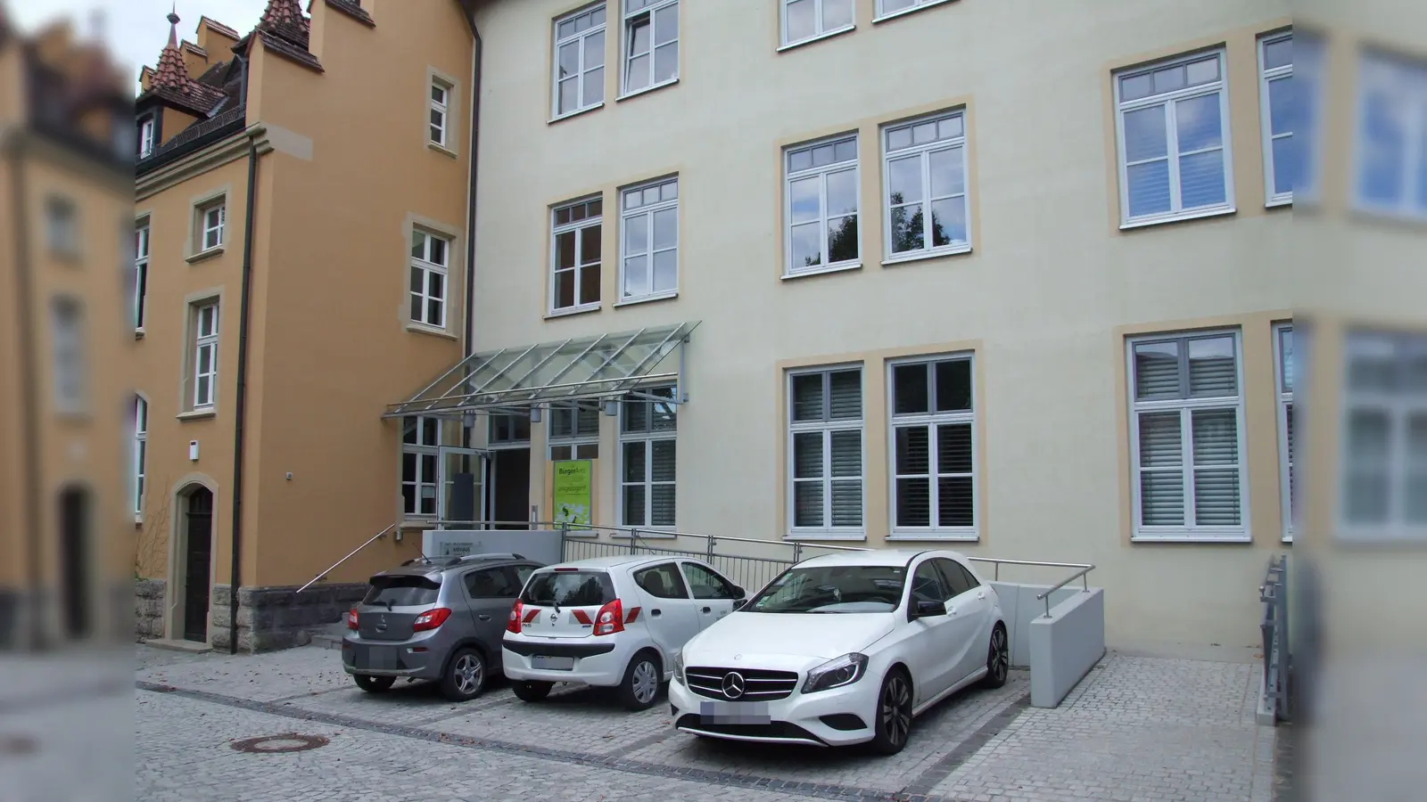 Das Erdgeschoss des Rathauses II ist über einen barrierefreien Aufgang zu erreichen, die anderen Stockwerke bislang nur über Treppen. Geplant ist die Errichtung eines Außenaufzugs. Diesem zum Opfer fallen würde der Parkplatz gleich an der Treppe.  (Foto: Jasmin Kiendl)
