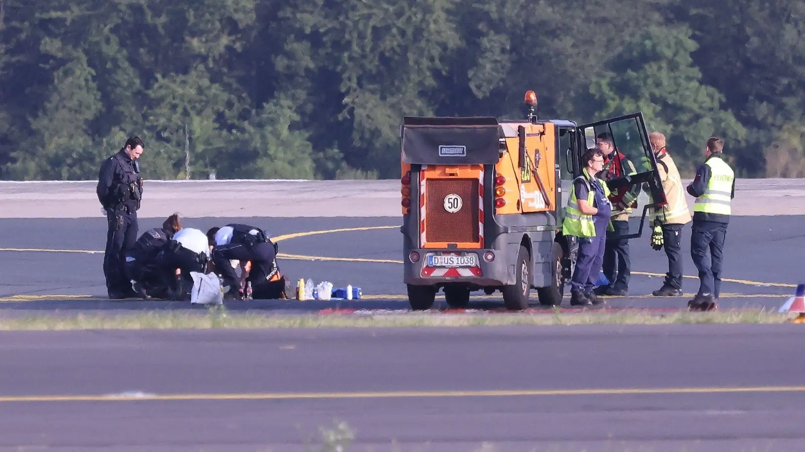 Sicherheitspersonal und Polizisten versuchen am Düsseldofer Flughafen, Aktivisten vom Asphalt auf dem Rollfeld zu lösen. (Foto: David Young/dpa)