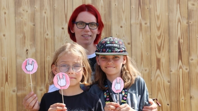 Mina (vorne rechts) verteilt ihre selbstgebastelten Pommesgabel-Schildchen an Metal-Fans. Sie ist gemeinsam mit ihrer Mutter Jessica Janitschek (hinten) und ihrer Schwester Lilly aus dem Odenwald angereist. (Foto: Antonia Müller)