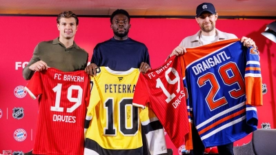 Fußball und Eishockey als Partner: Die deutschen Eishockeystars John-Jason Peterka (l) und Leon Draisaitl (r) mit dem kanadischen Bayern-Profi Alphonso Davies.   (Foto: Matthias Balk/dpa)