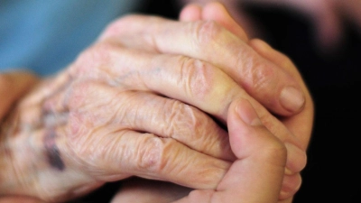 Eine Pflegekraft hält in einem Seniorenheim die Hand einer Bewohnerin. Die Pflegeversicherung sieht sich mit einem Defizit konfrontiert. (Foto: Daniel Reinhardt/dpa)