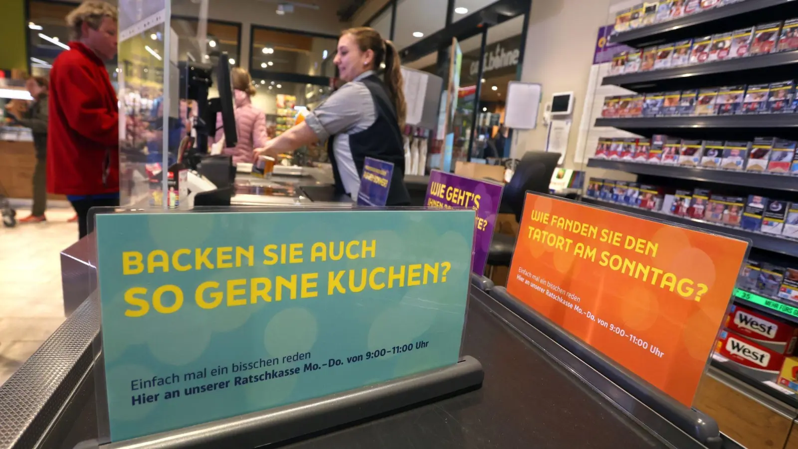 Eine Kassiererin steht mit einem Kunden bei der Eröffnung einer „Ratschkasse“ (Plauderkasse) in einem Edeka-Markt in Buxheim. (Foto: Karl-Josef Hildenbrand/dpa)