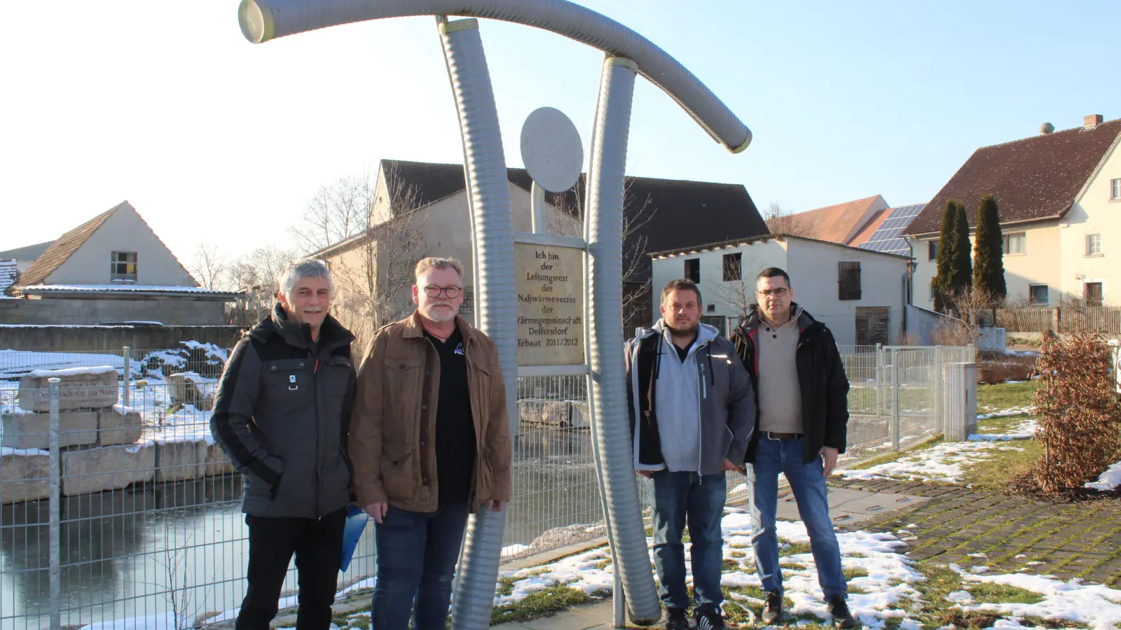 Aus den Leitungsresten des Nahwärmenetzes haben die Protagonisten Herbert Grießer, Christian Bear, Markus Deffner und Robert Kral (von links) ein „Erinnerungsdenkmal“ in der Mitte des 20 Anwesen umfassenden Dorfes errichten lassen. (Foto: Herbert Dinkel)