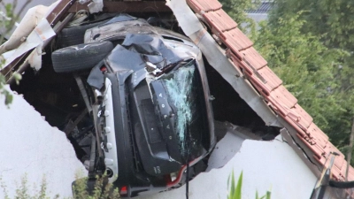Ein Auto liegt nach einem kurzen Flug seitlich in der Mauer einer Scheune. (Foto: -/Moonshine Media/dpa)