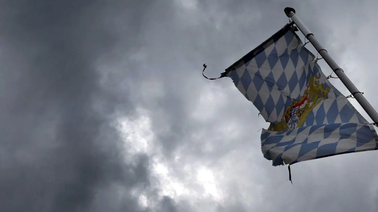 Eine Bayernfahne weht vor dichten Regenwolken im Wind. (Foto: Karl-Josef Hildenbrand/dpa)