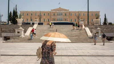 Eine Frau schützt sich mit einem Sonnenschirm  auf dem Syntagma-Platz in Athen vor der Sonne: Warme Luftmassen sorgen für Temperaturen von örtlich bis zu 45 Grad. (Foto: Socrates Baltagiannis/dpa)