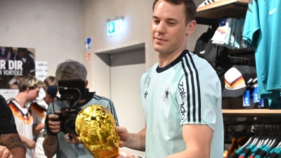 Lächelnd signiert Manuel Neuer einen goldenen WM-Pokal.  (Foto: Federico Gambarini/dpa)
