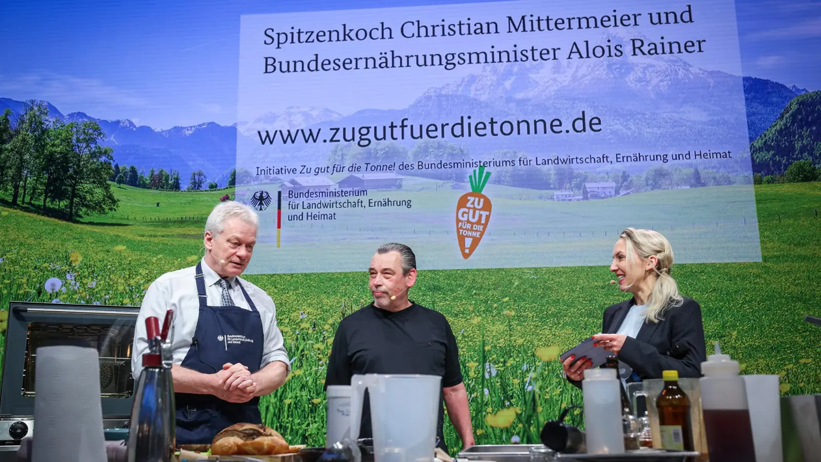Bundesminister Alois Rainer (links) und Christian Mittermeier beim gemeinsamen Kochen. Mit im Bild ist Moderatorin Carolin Kuhn.  (Foto: Ronny Hartmann / BMLEH)