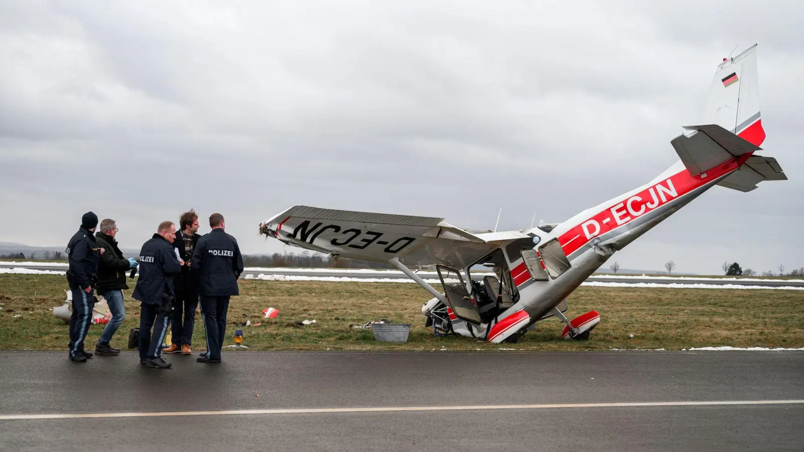 Die ermittelnden Polizeibeamten stehen neben dem verunglücktem Kleinflugzeug  Cessna auf dem Flugplatz in Coburg. (Foto: Daniel Vogl/dpa)