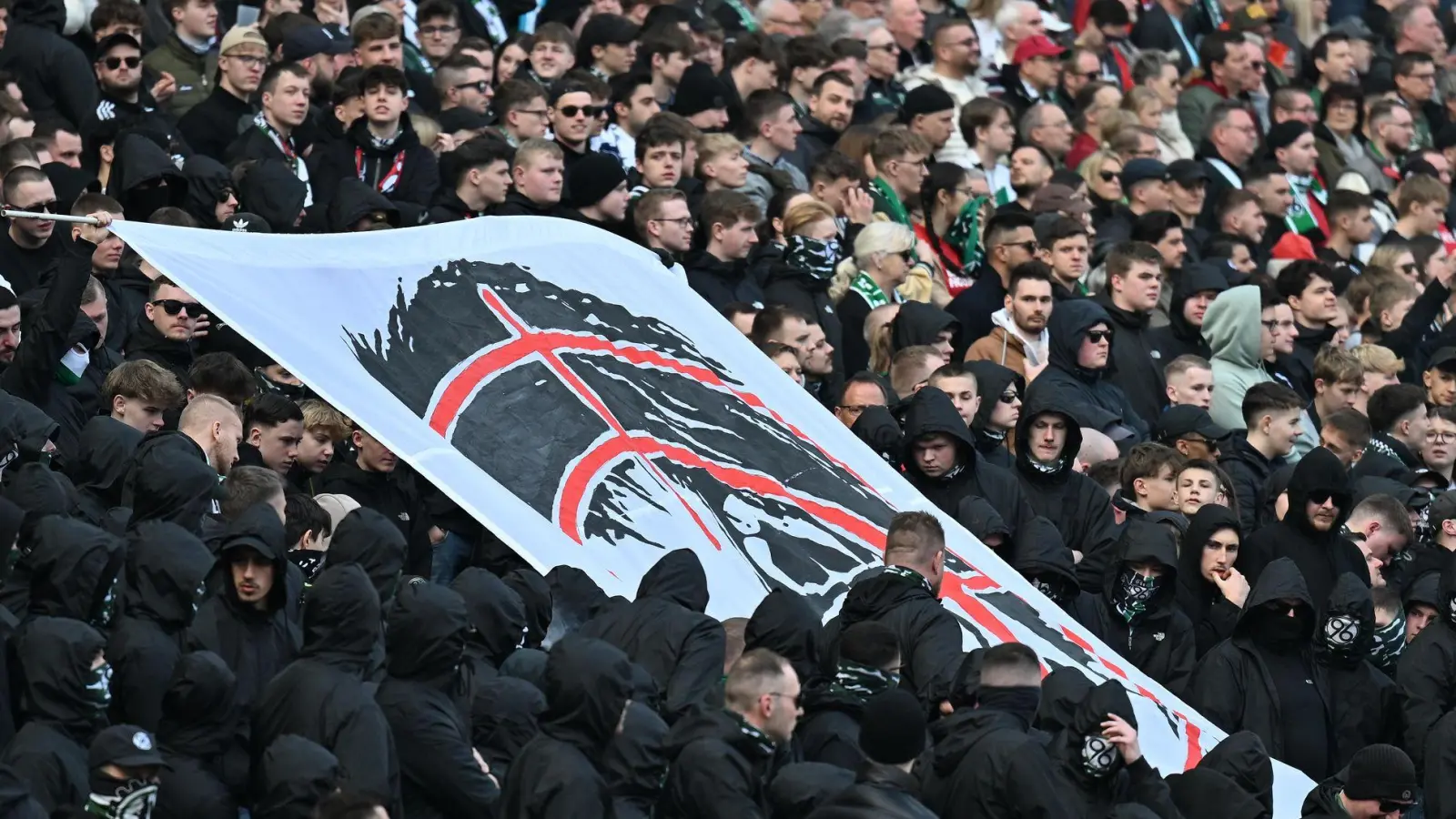 Hannover-Fans halten auf der Tribüne ein Plakat hoch, dass den Kopf von Niedersachsens Innenministerin Daniela Behrens in einem Fadenkreuz zeigt. (Foto: Swen Pförtner/dpa)