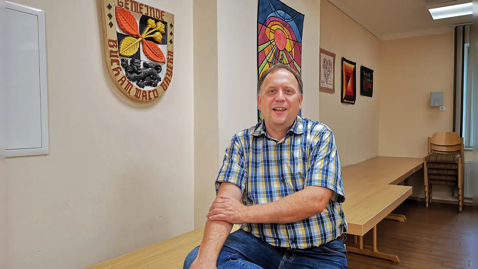 Mit seiner Rolle als ehrenamtlicher Bürgermeister von Buch am Wald kommt Hartmut Buckel gut klar. Das Foto zeigt ihn im Sitzungssaal neben dem Gemeindewappen. (Foto: Jürgen Binder)