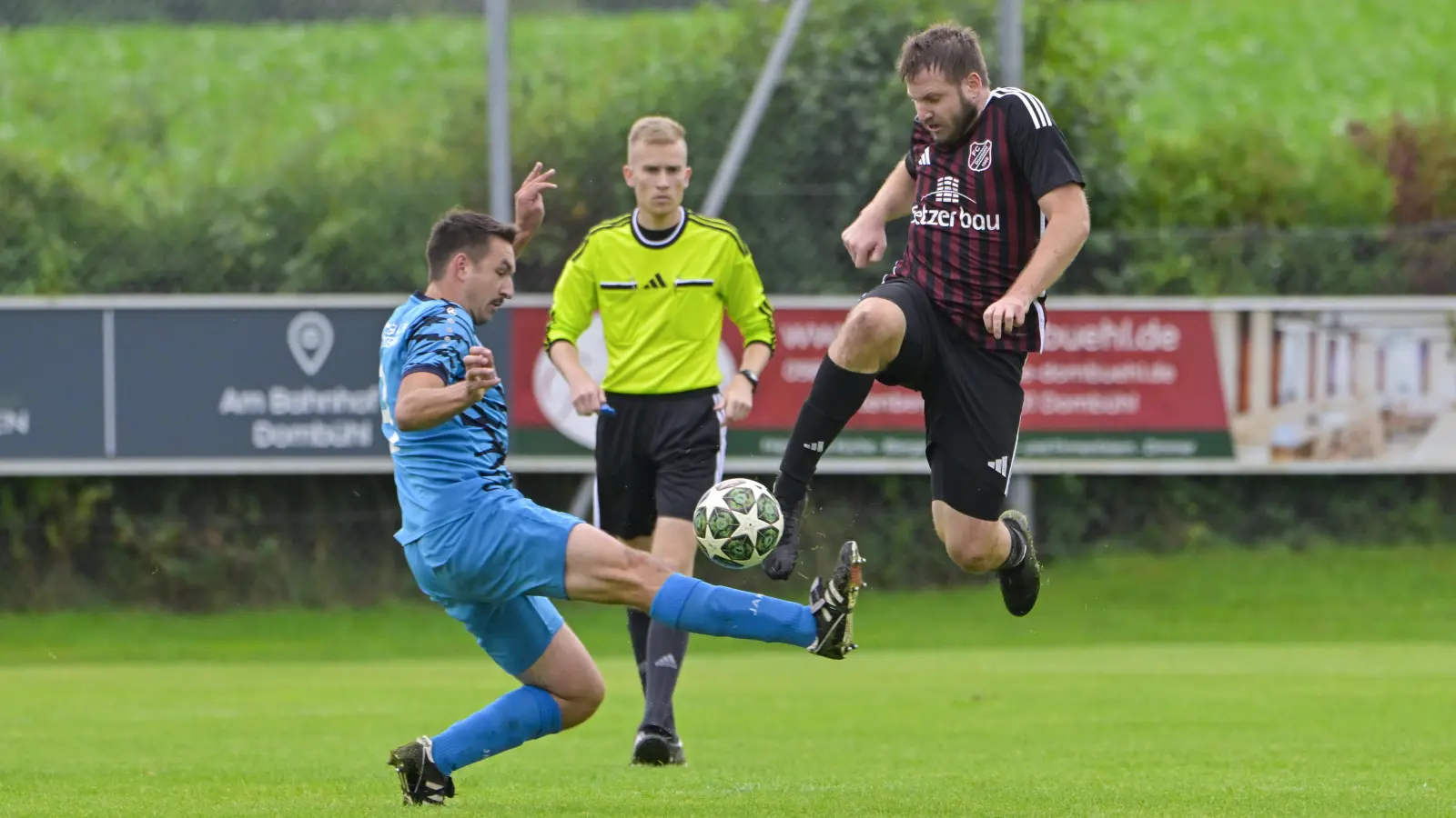 Wenn das mal nicht einem der beiden Spiele weh tut: Tom Wassermann von der SG Mosbach-Breitenau spritzt gegen Alexander Häßlein vom FC Dombühl dazwischen. Schiedsrichter Simon Dimmerling schaut genau hin. (Foto: Martin Rügner)