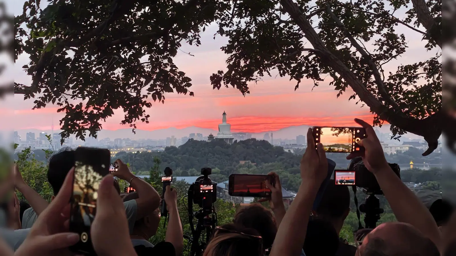 Touristen fotografieren mit ihren Handys den farbenfrohen Sonnenuntergang über der chinesischen Hauptstadt. (Foto: Xing Guangli/XinHua/dpa)