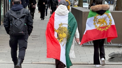 Menschen, die verschiedene ehemalige Flaggen des Iran umhaben, gehen durch die Münchner Innenstadt. (Foto: Marijan Murat/dpa)