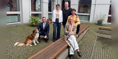 Im Innenhof des Gymnasium Carolinum, der zu den Spielorten des Wandeltheaterstücks gehört: Regisseurin Daniela Aue (vorne) sowie der Schauspieler Lukas Aue, der Komponist Stefan Kammerer, Chorleiterin Franziska Argmann und Schulleiter Stefan Exner (hinten von rechts). Daniela Aues Hund Elmo ist bei den Proben dabei.  (Foto: Lara Hausleitner)