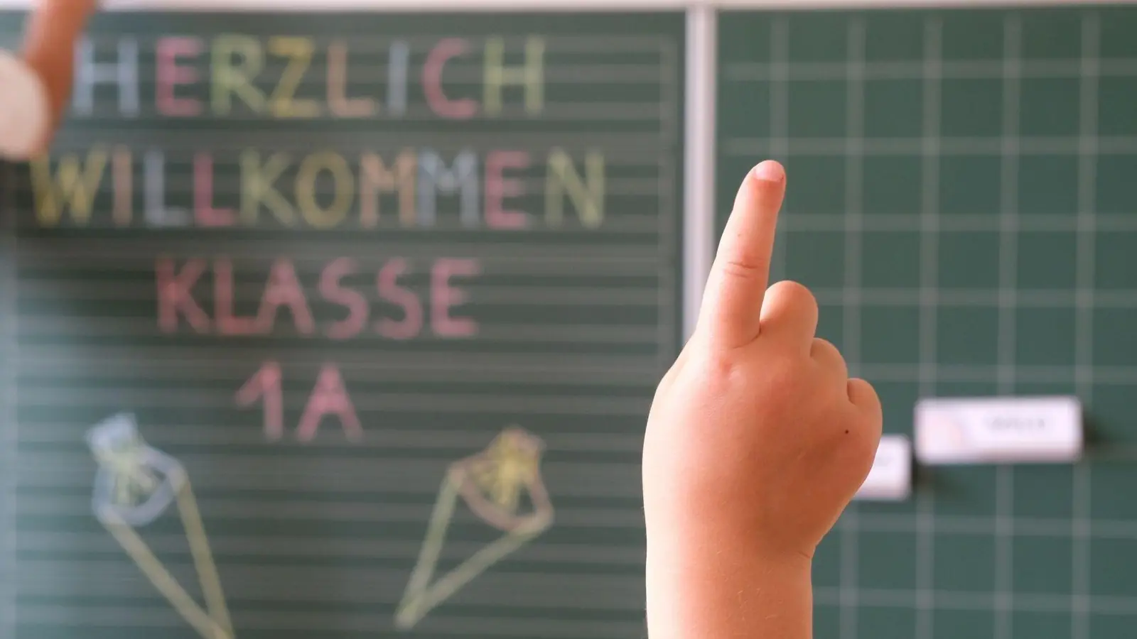 „Herzlich willkommen Klasse1 A“ steht an der Tafel eines Klassenzimmers, während sich ein Kind meldet. Am Samstag wird in Sachsen Einschulung gefeiert. (Foto: Sebastian Willnow/dpa)