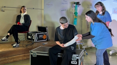 Mia Sophie Schneider, Nisa Sat und Niklas Lang aus der 11. Klasse Sozialwesen FOS Ansbach (v. rechts) zeigen den Alltag in der Notaufnahme einer Klinik. Links im Hintergrund Claudia Fritzsche (ANregiomed), die vor der Szene auf der Bühne über ihren Alltag in der Akutpflege berichtet hatte. (Foto: FOSBOS Ansbach)