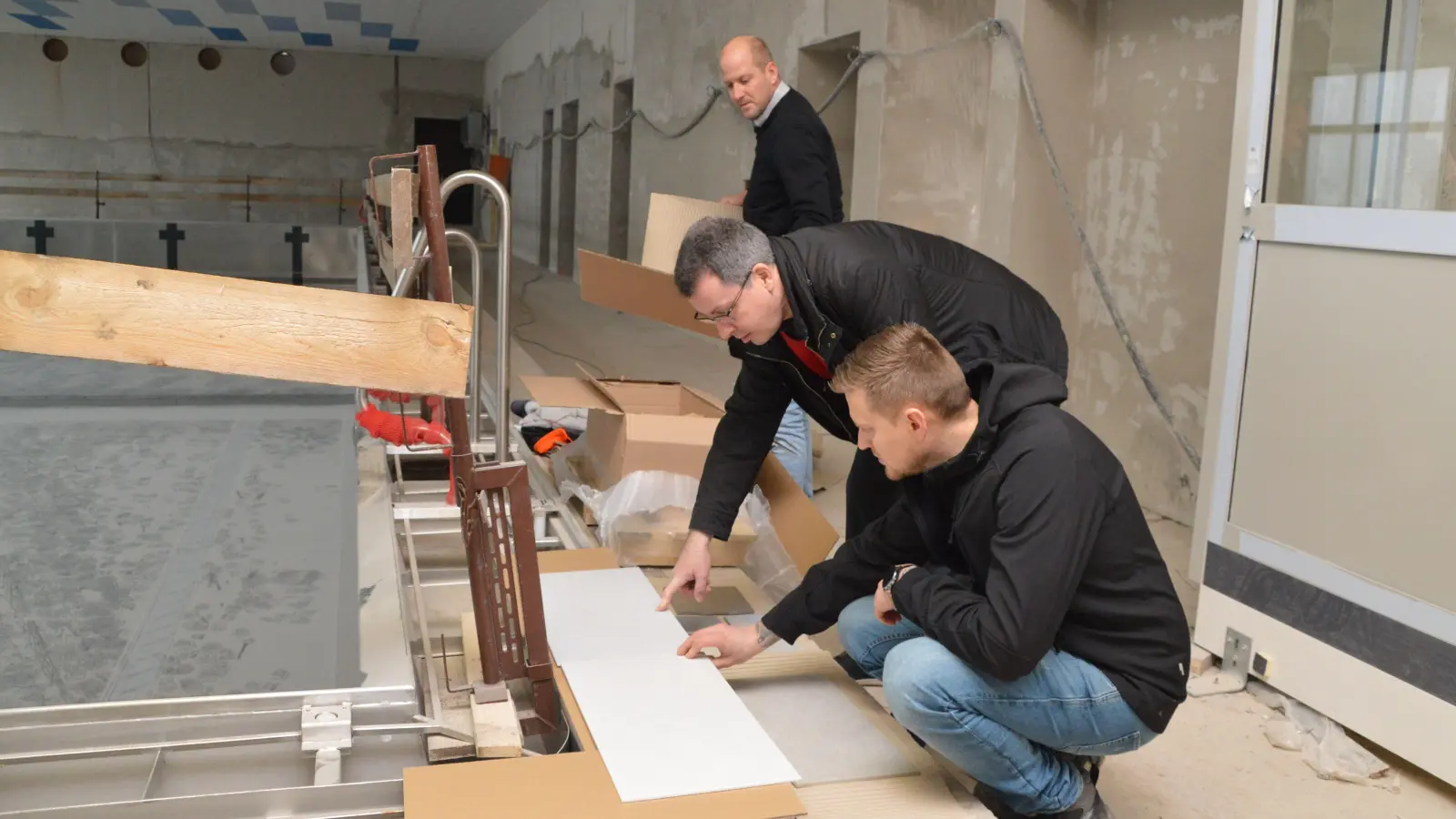 Im Uffenheimer Hallenbad sind Musterfliesen angekommen: Hochbauamtsleiter Viktor Scheider und Bürgermeister Wolfgang Lampe (Mitte) beraten, während Stadtbaumeister Jürgen Hofmann (hinten) auspackt. (F.: J. Zimmermann)