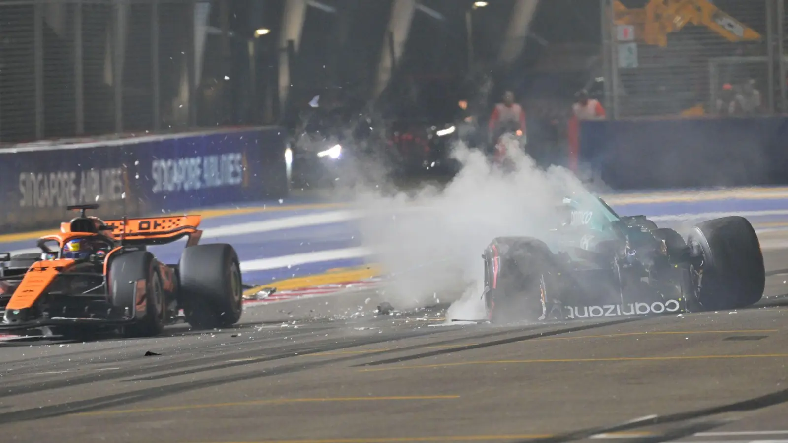 Nach einem Unfall steigt aus dem Auto von Lance Stroll (r) Rauch auf, während Oscar Piastri an der Unfallstelle vorbeifährt. (Foto: Caroline Chia/Reuters Pool/AP/dpa)