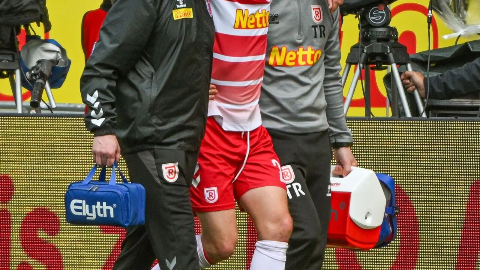 Elias Huth (M) von Regensburg wird verletzt vom Platz geführt. (Foto: Armin Weigel/dpa)