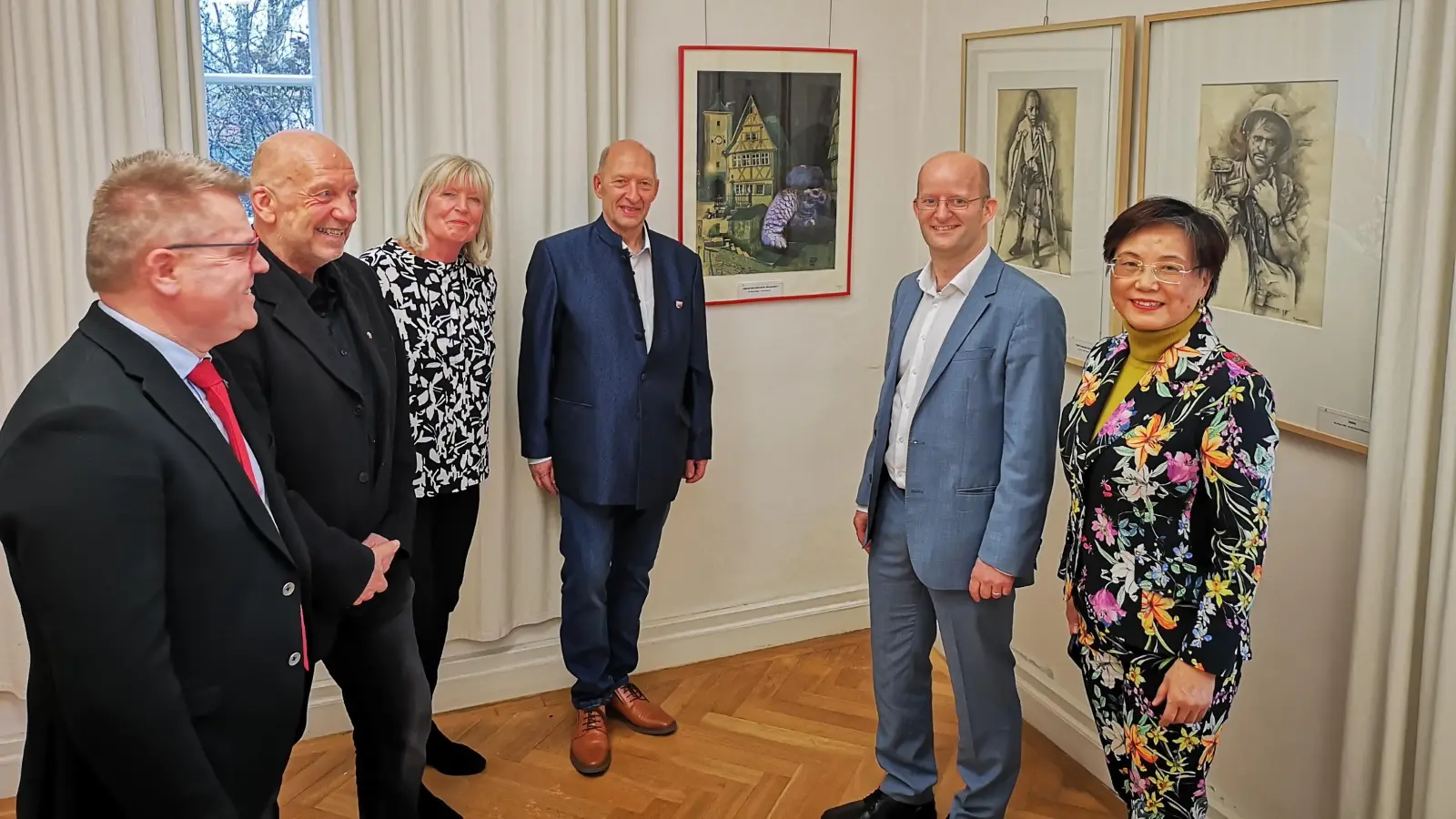 Die erste Sonderschau des Jahres 2024 im Schillingsfürster Doerfler-Museum ehrt das Lebenswerk des Rothenburgers Robert Hellenschmidt. Das Foto zeigt (von rechts) Leiterin Hai Yan Waldmann-Wang mit dem Rothenburger OB Dr. Markus Naser, dem Schillingsfürster Rathauschef Michael Trzybinski, der Witwe des Künstlers, Hildegard Hellenschmidt, Markus Löschel und dem stellvertretenden Landrat Stefan Horndasch – im Hintergrund drei Arbeiten des Künstlers, die beweisen, dass sich sein kreatives Schaffen nicht auf Karikaturen beschränkte. (Foto: Jürgen Binder)