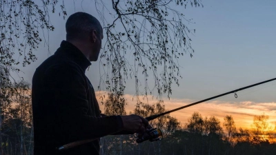 Ein Angler steht bei Sonnenaufgang an einem Teich in Brandenburg. (Foto: Frank Hammerschmidt/dpa)