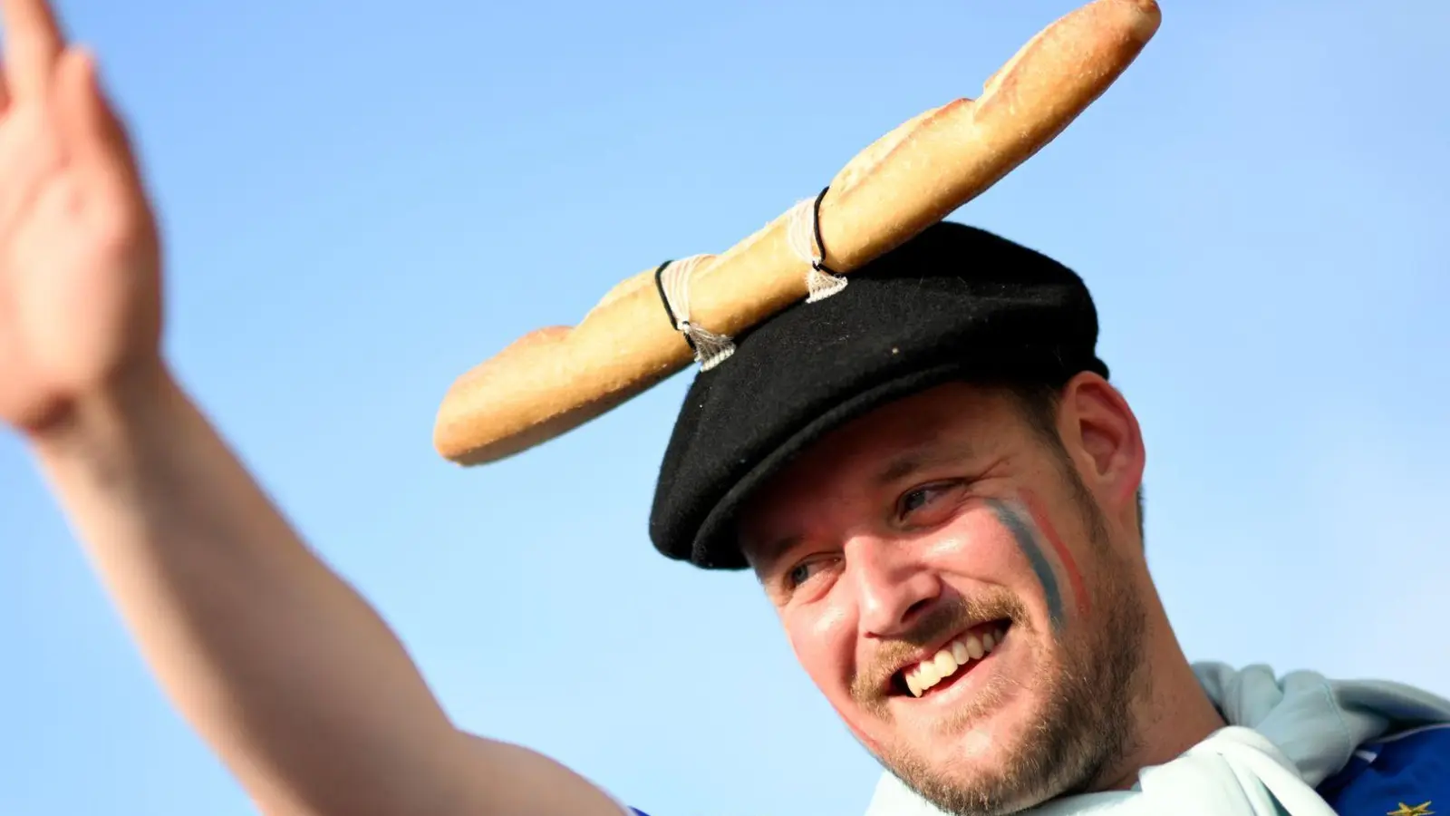 Das Baguette ist eines der großen Symbole Frankreichs. Man kann es essen - oder auch mal an der Mütze befestigen. Dieser Fan freut sich in Düsseldorf auf das EM-Spiel gegen Österreich. (Foto: Fabian Strauch/dpa)