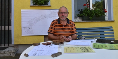 Günther Rabenstein, Obmann der Osing-Verwaltung und Hüter der Traditionen, bei sich zu Hause in der Modelsmühle: Versteinertes Holz vom Osing beschwert vor ihm das Papier. (Foto: Anita Dlugoß)