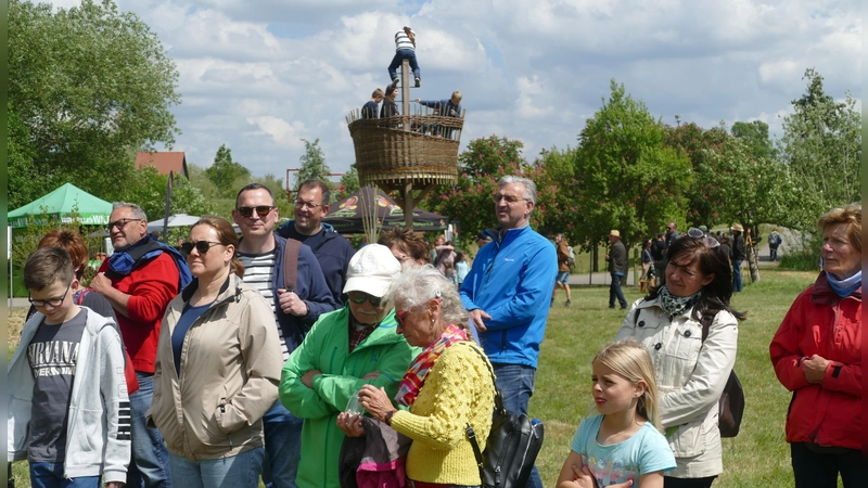 Die Teilnehmer eines Rundgangs durch die Streuobstwiesen schauen sich Kokons der Seidenraupe an. Im Hintergrund ist das Krähennest zu erkennen, ein Spielturm, der bei Kindern sehr beliebt ist. (Foto: Helmut Meixner)