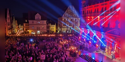 Stimmungsvoller geht es nicht: Während die letzten Gruppen mit ihren Fackeln von der Schmiedgasse am Marktplatz eintreffen, haben alle anderen schon Aufstellung vor dem prächtig illuminierten Rathaus genommen. Eine enorme Menschenmenge verfolgt das Geschehen. (Foto: Jürgen Binder)