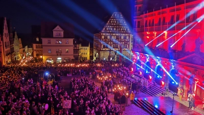 Stimmungsvoller geht es nicht: Während die letzten Gruppen mit ihren Fackeln von der Schmiedgasse am Marktplatz eintreffen, haben alle anderen schon Aufstellung vor dem prächtig illuminierten Rathaus genommen. Eine enorme Menschenmenge verfolgt das Geschehen. (Foto: Jürgen Binder)