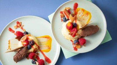 Sieht aus wie ein Bagel aus Eis: In sogenannte Savarin-Formen wird das Mangoeis gefüllt und gefroren. Die Mitte wird mit Fruchtigem gefüllt, dazu einen Klecks Schokoladenmousse, Mango- und Erdbeerpüree drunter und drüber streichen. (Foto: Christin Klose/dpa-tmn)