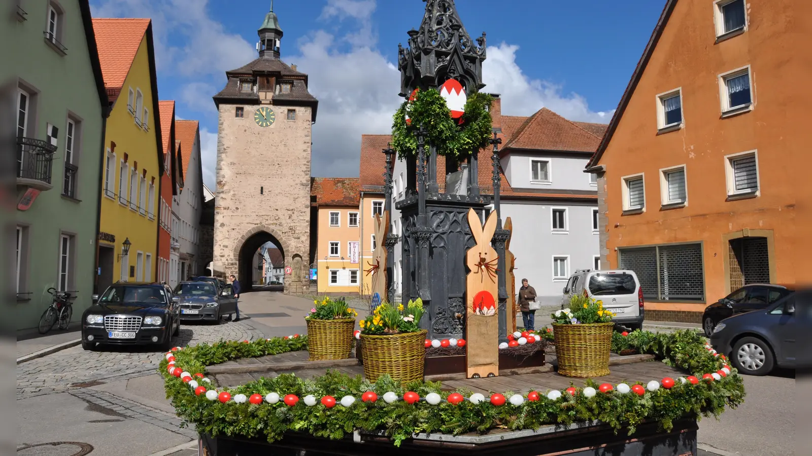 Den Röhrenbrunnen vor dem Rathaus von Leutershausen hat der Heimatverein mit Osterschmuck versehen. Selbstgebundene Girlanden mit rot-weißen Eierketten, Osterhasen aus Holz und Weidenkörbe, hergestellt vom Leutershäuser Korbmacher und mit Frühlingsblumen bepflanzt von der heimischen Gärtnerei, schmücken ihn. Es gab auch eine kleine Feier, bereichert durch fröhliche Lieder des Kinderchores unter der Leitung von Kathrin Albrecht und Barbara Reinert. Gemeinsam sangen die Teilnehmer „Alle Vöglein sind schon da“. Die Chorkinder freuten sich über gefüllte Nester und die Zuhörer über ein buntes Osterei. Kräftige Regenschauer verscheuchten die Gäste in den überdachten Biergarten des Wirtshauses vis-a-vis. Der ursprünglich aus der Fränkischen Schweiz stammende Brauch wird in Leutershausen seit 2004 gepflegt.  (Foto: Wolfgang Grebenhof)