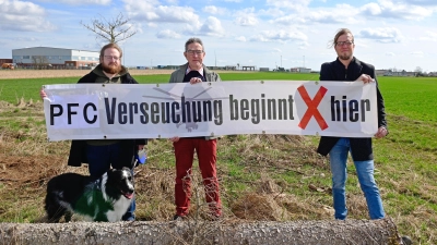 Sie fordern, dass endlich der PFC-Hotspot in der Katterbacher Kaserne angegangen wird (von links): André Fitzthum mit Hund Oskar, Wolfgang Schmidt und Boris-André Meyer von der Bürgerinitiative „Etz langt’s“. Im Hintergrund ist die Baustelle für die Abstromsicherung zu erahnen. (Foto: Alina Boger)