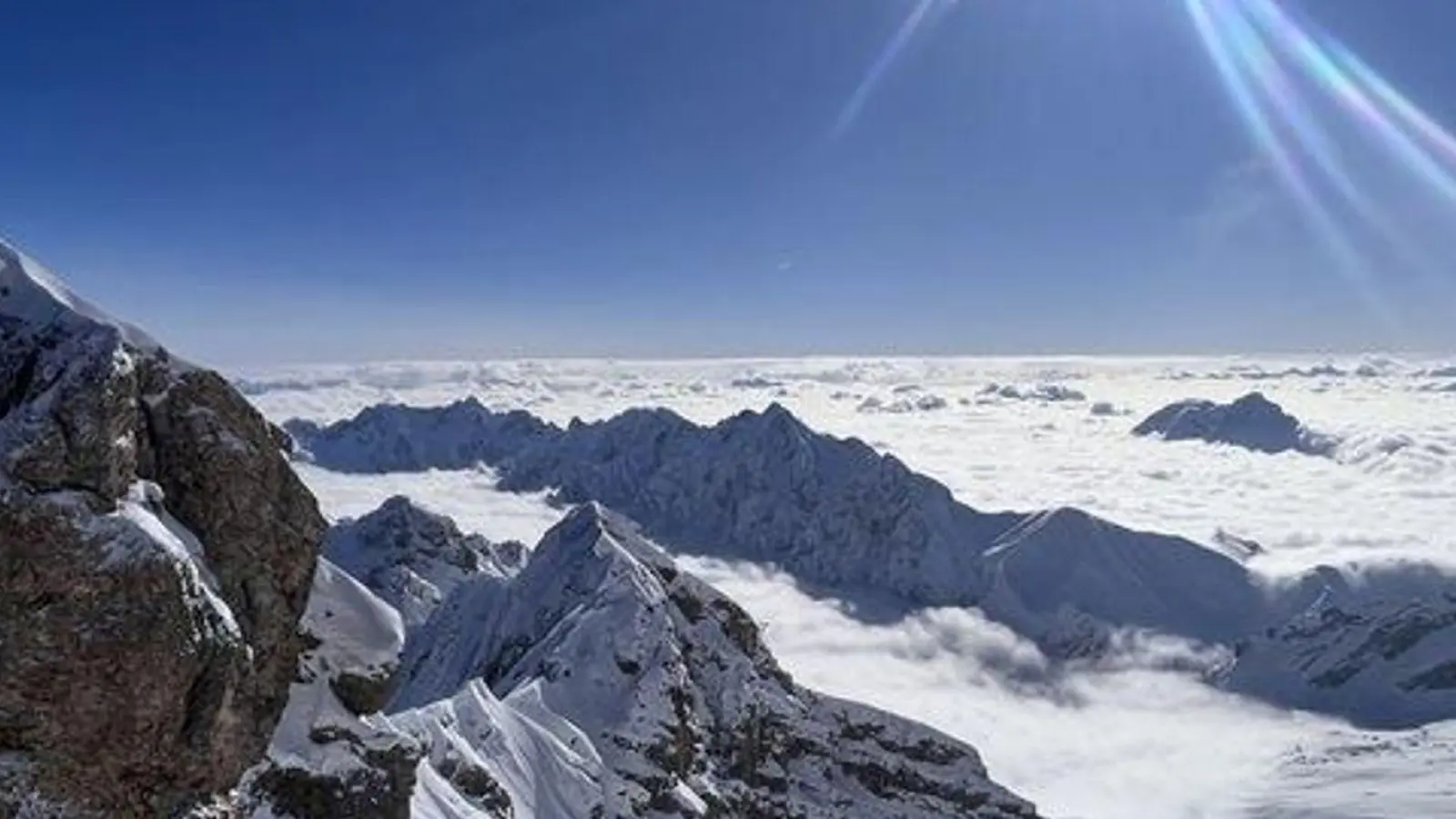 Die Sonne scheint über dem Gipfelkreuz der schneebedeckten Zugspitze. (Foto: Christoph Trost/dpa)