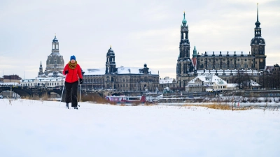 Eine Frau läuft am verschneiten Elbufer vor der historischen Altstadtkulisse in Dresden Ski (Foto: Robert Michael/dpa)