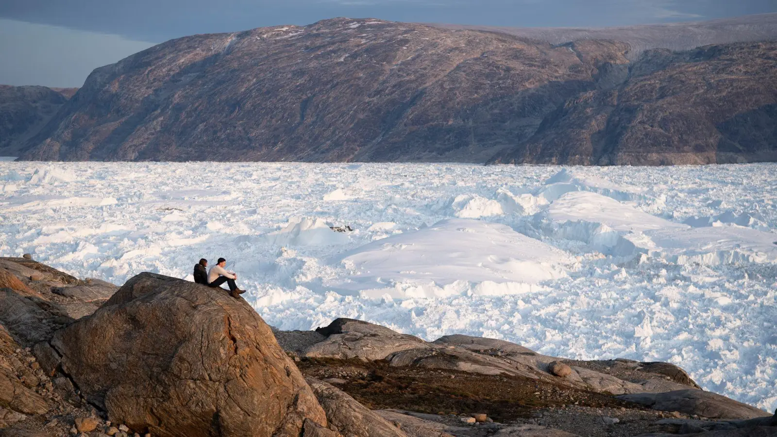 Zwei Studenten der New York University sitzen auf einem Felsen mit Blick auf den grönländischen Helheim-Gletscher.  (Foto: Felipe Dana/AP/dpa)