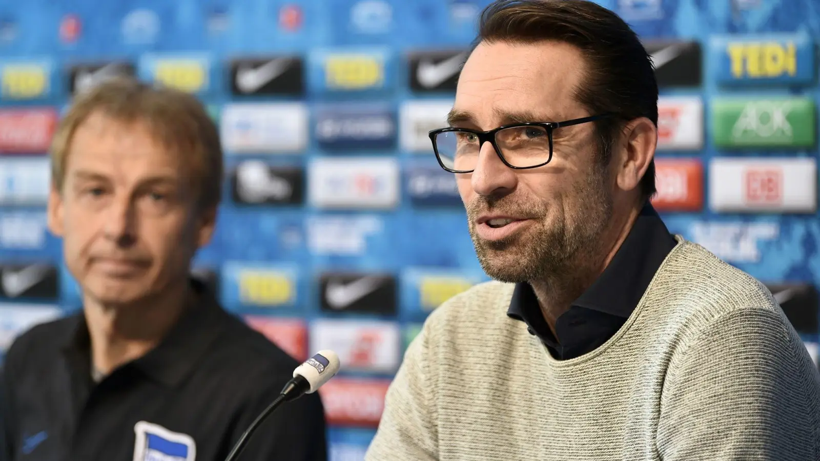 Jürgen Klinsmann (l) verfolgt die Worte von Michael Preetz, dem damaligen Geschäftsführer von Hertha BSC. (Foto: Sven Braun/dpa)