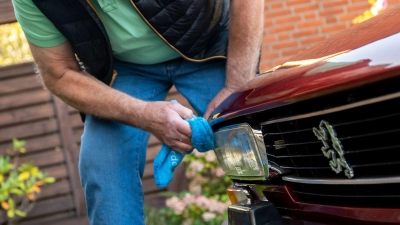 Ein Mann reinigt die Scheinwerfer seines Peugeot 504 Coupé-Oldtimers. Unter Umständen kann man das Licht auf modernes LED-Licht aufrüsten, ohne den Oldtimerstatus zu verlieren. (Foto: Benjamin Nolte/dpa-tmn/dpa)