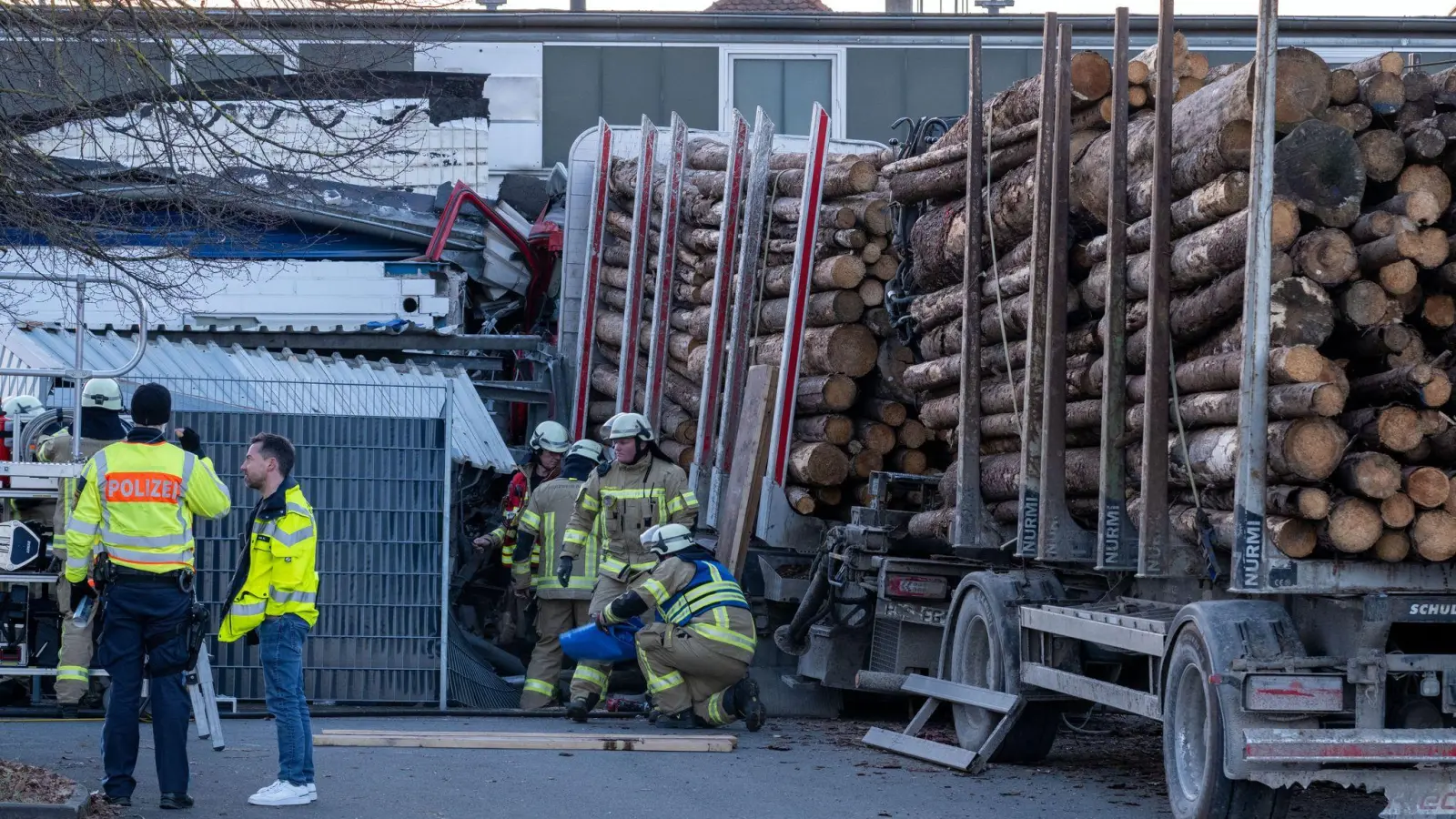 Ein Holzlaster steckt mit dem Führerhaus in einem Gebäude. Die Polizei geht davon aus, dass der Fahrer wegen eines medizinischen Notfalls die Kontrolle über den Laster verlor. (Foto: Pia Bayer/dpa)