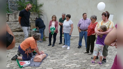 „Das ist ja ganz schön anstrengend so eine Herzdruckmassage“ , stellte eine Adelsdorferin (kniend) fest, die unter Anleitung von Ludwig Winter (links), Silvia Heubeck (Mitte) und Claudia Wust (Dritte von links) versuchte, den Patienten – in diesem Fall eine lebensgroße Puppe – mit Hilfe eines Defibrillators am Leben zu erhalten. (Foto: Sylvia Fehlinger)