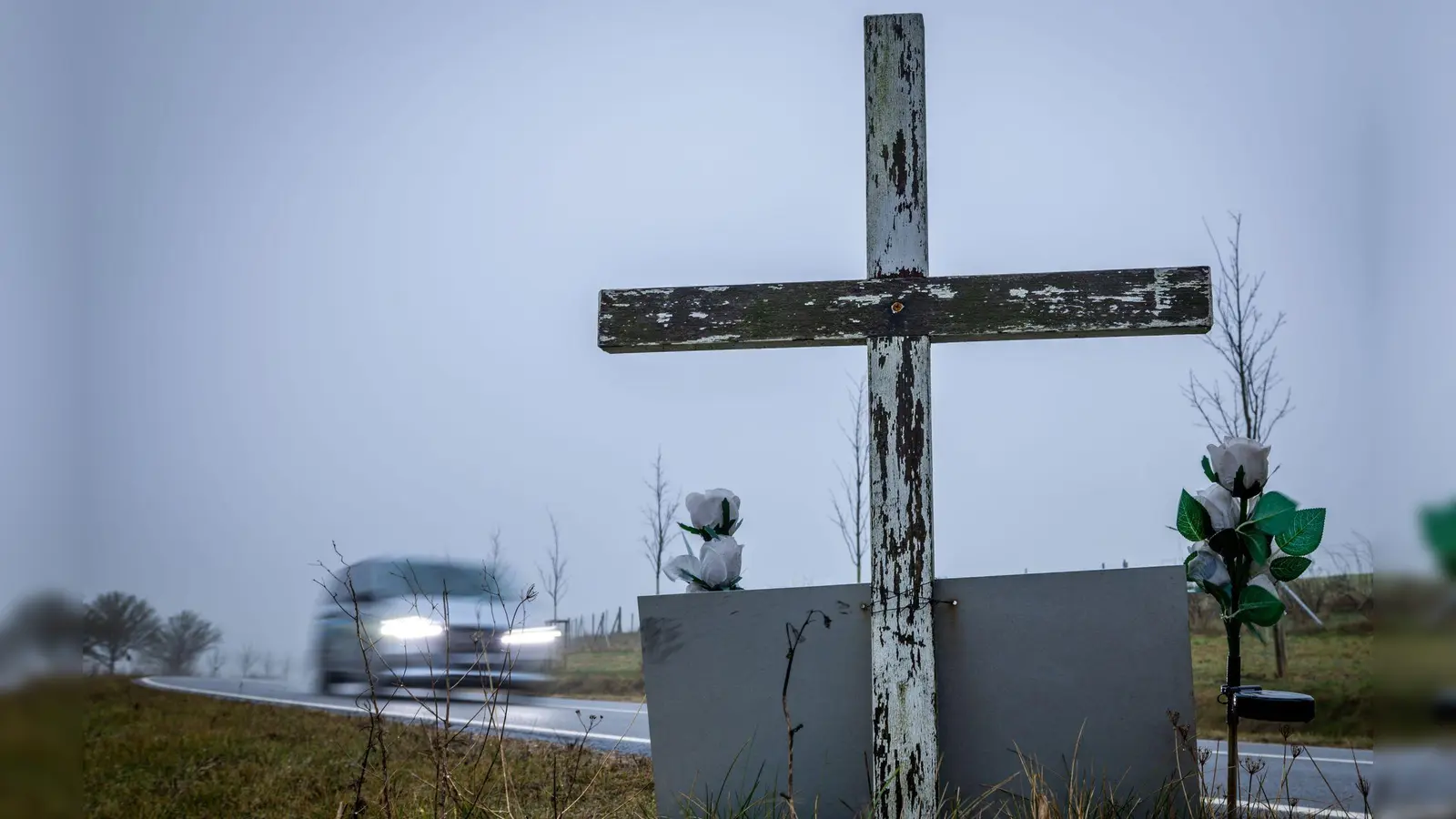 in Auto fährt auf einer Landstraße an einem hölzernen Kreuz vorbei, welches zur Erinnerung an ein Unfallopfer aufgestellt wurde. (Foto: Jens Büttner/dpa)