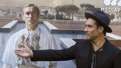 Jude Law vor einem Plakat mit sich als Papst Pius XIII. in der Serie „The Young Pope“. (Archivbild) (Foto: picture alliance / dpa)