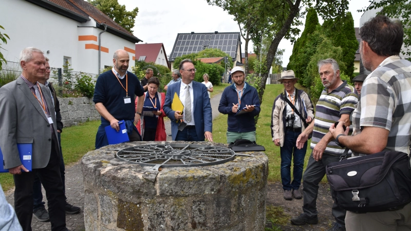 Unter diesem Brunnen ist die Wieseth-Quelle verborgen. Eduard Hillermeier (Zweiter von rechts) erläutert der Jury im Bezirksentscheid und Gästen wie Bezirksrat Herbert Lindörfer (Bildmitte) die Pläne zur Verschönerung. (Foto: Silvia Schäfer)
